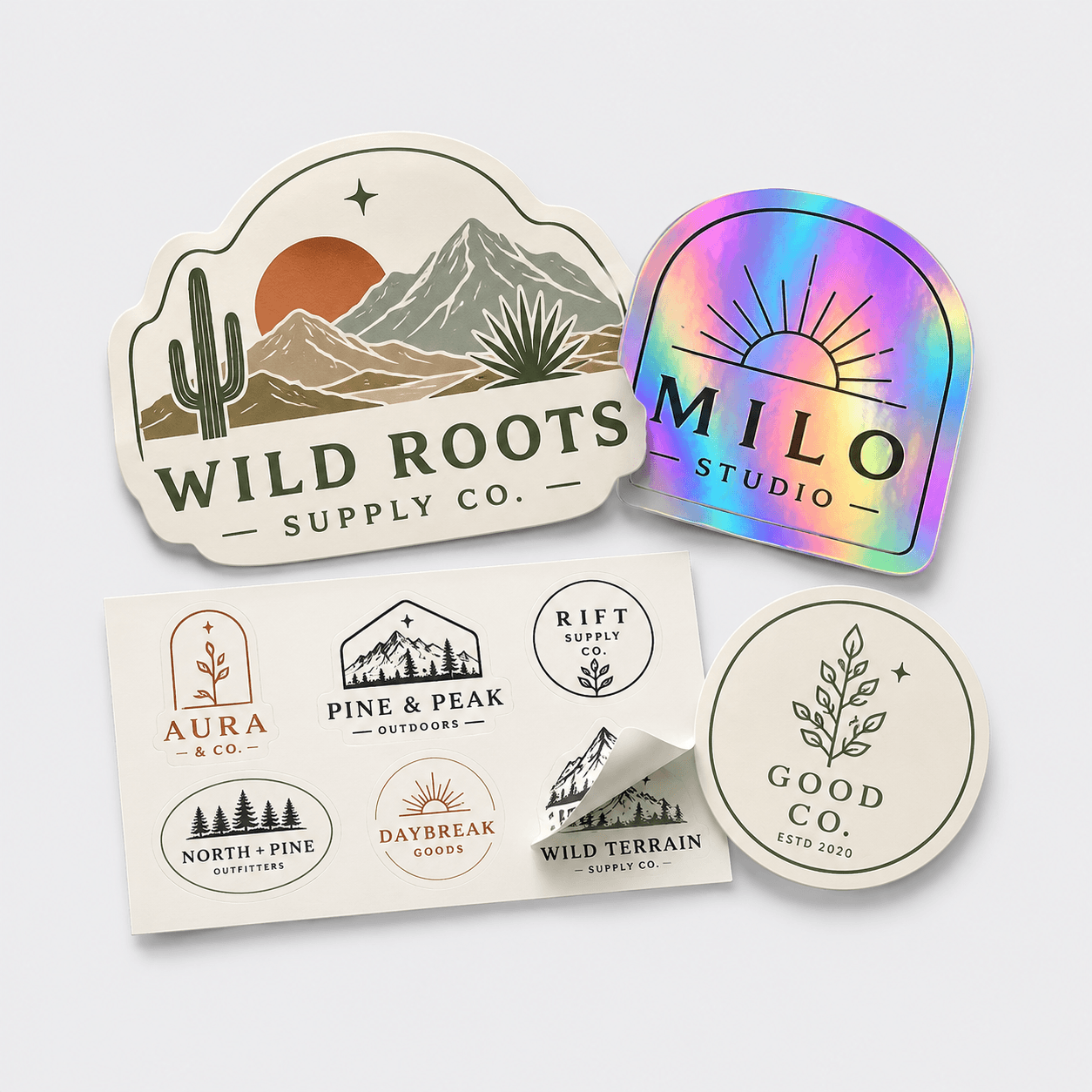 Custom stickers in four formats: die-cut WILD ROOTS badge, holographic MILO Studio, kiss-cut sticker sheet with peel detail, and a GOOD CO. circle sticker on a clean studio background